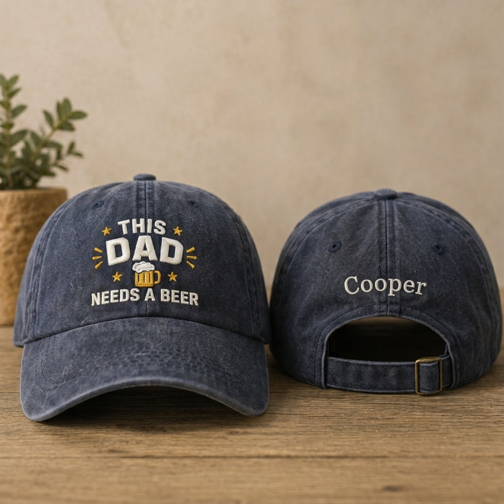 Two denim baseball caps on a wooden surface with one displaying 'This Dad Needs a Beer' text and the other with 'Cooper' embroidered.
