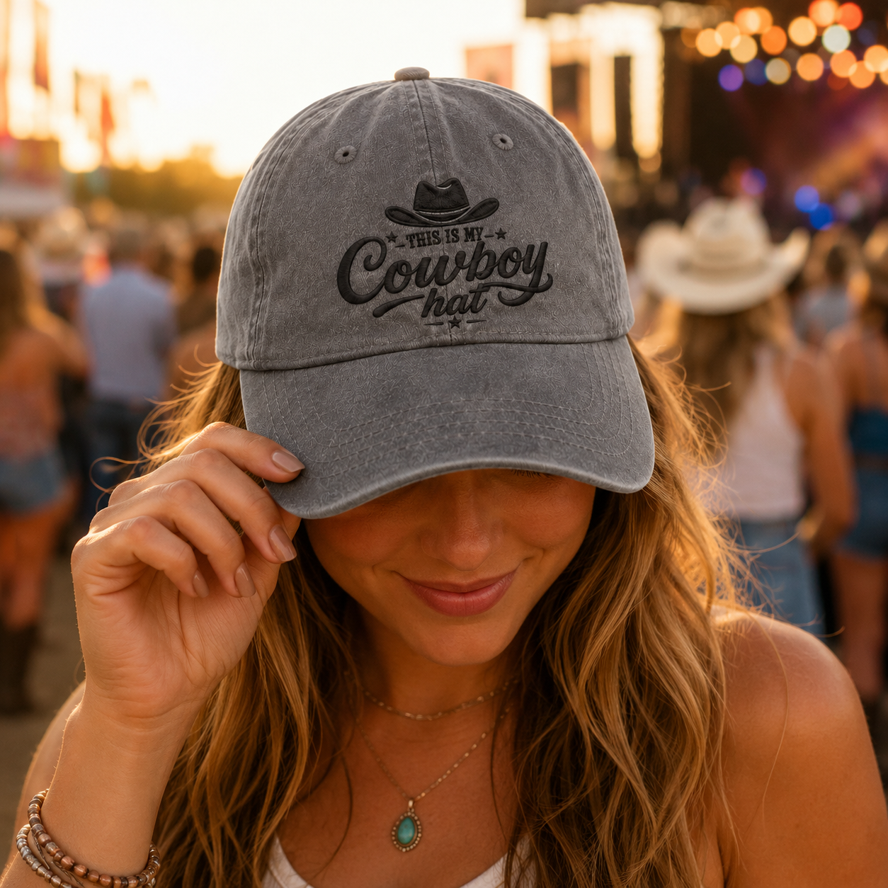 Grey washed cotton baseball cap with embroidered western cowboy text worn by a woman at a country concert