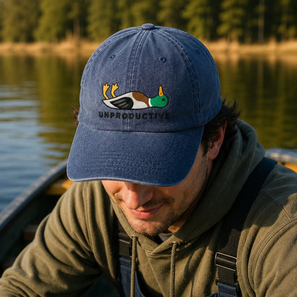 Man wearing a blue cap with a duck design and 'UNPRODUCTIVE' text, sitting in a boat by a lake.