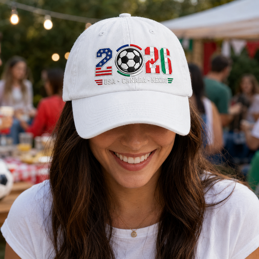 Woman smiling at a watch party wearing a white washed baseball cap with embroidered 2026 tri-country soccer game day design