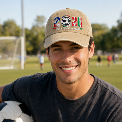 Man smiling on a soccer field wearing a sand washed baseball cap with embroidered 2026 North American tournament soccer ball design