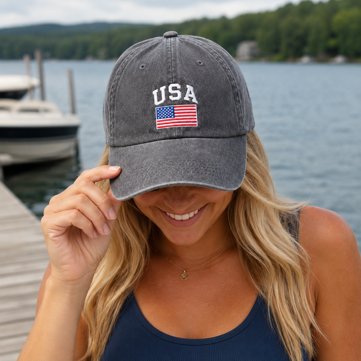 Woman by a lake dock adjusting a grey washed baseball cap with an embroidered USA flag design
