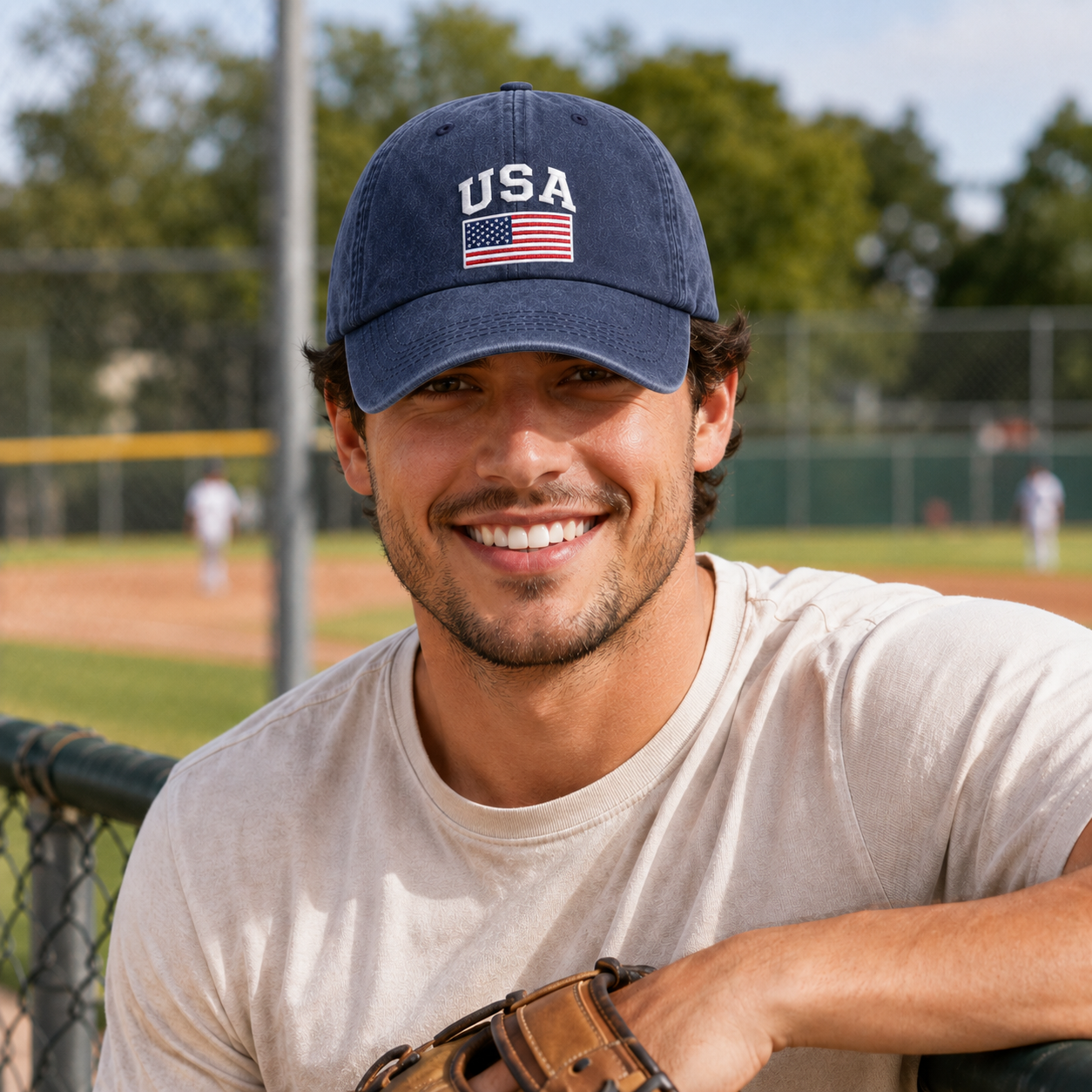Man smiling at a baseball field dugout wearing a navy washed baseball cap with an embroidered USA flag design