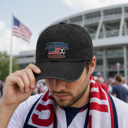 Man wearing a patriotic scarf outside a stadium and adjusting a black washed baseball cap with an embroidered America 2026 soccer and US flag design