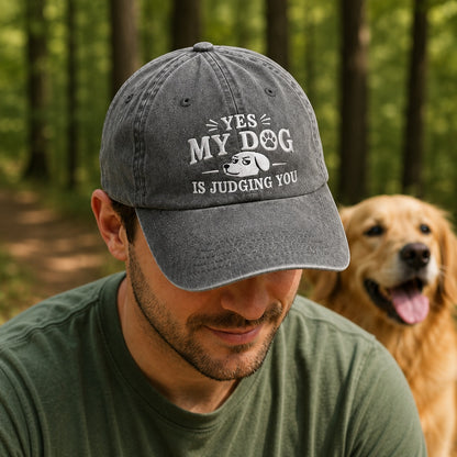 Man wearing a cap with 'Yes, my dog is judging you' text in a forest setting with a dog.