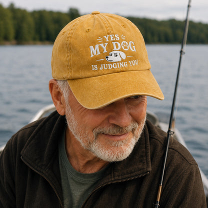 Man on a boat wearing a yellow cap with text and a dog graphic, with water and trees in the background.