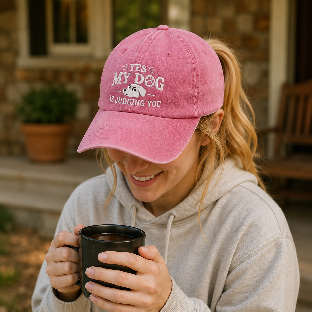 Woman wearing a pink cap with text and holding a mug outdoors.